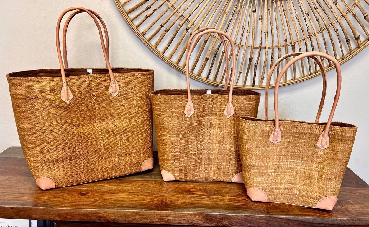 Three woven handbags with leather handles on a wooden surface.
