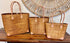 Three woven handbags with leather handles on a wooden surface.
