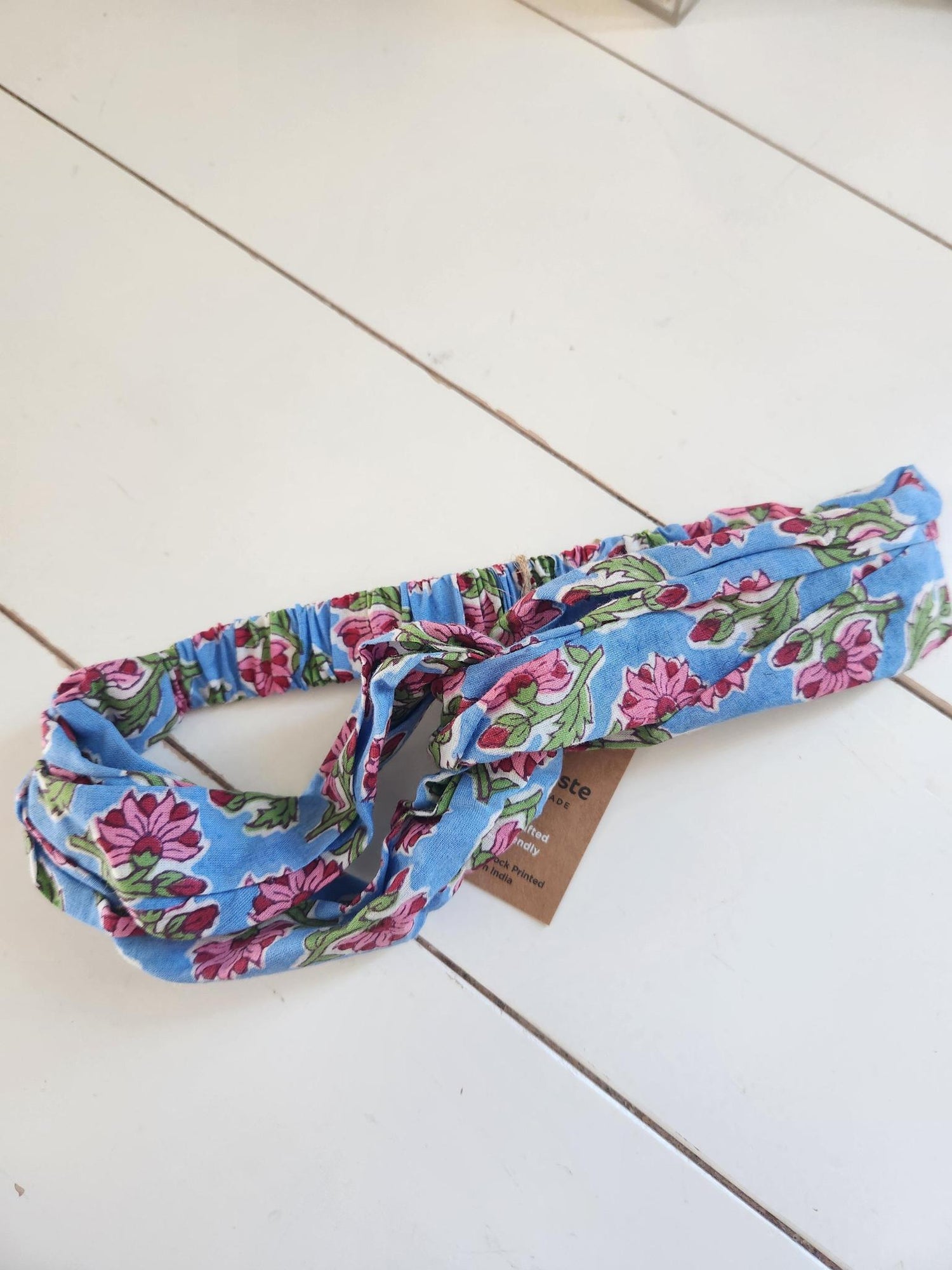Blue headband with pink and green flowers on a white wooden surface