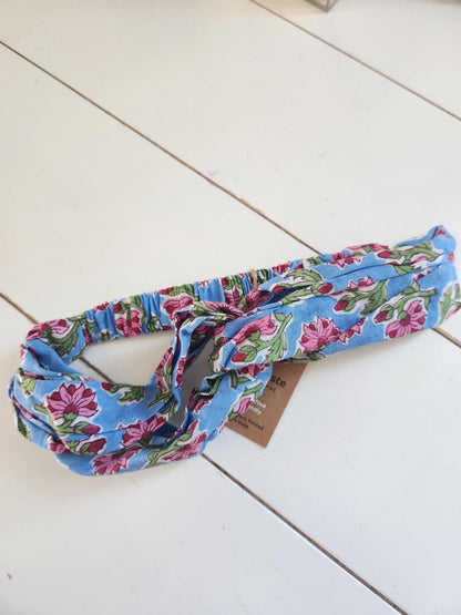 Blue headband with pink and green flowers on a white wooden surface