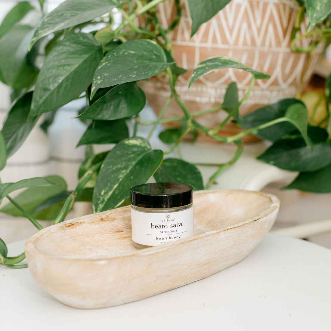 Jar of beard salve on a wooden tray with plants in the background