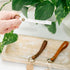 Three leather keychains. One being held and the others on a wooden plate with a plant in the background