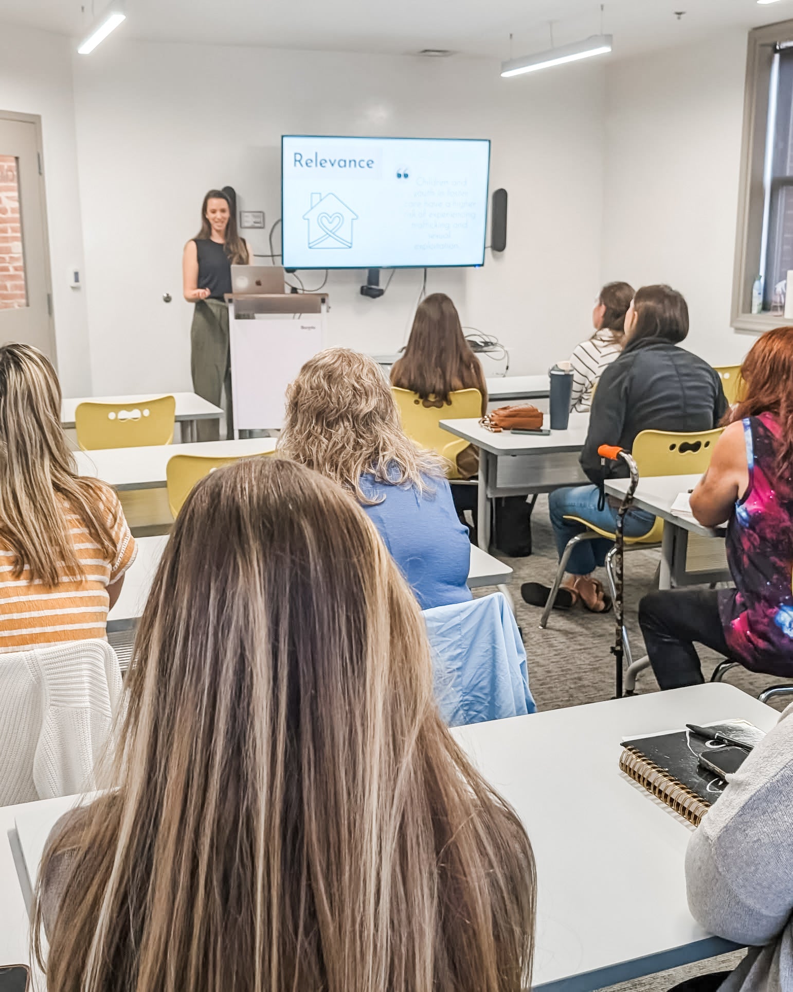 Person giving a presentation in a classroom setting with students seated.