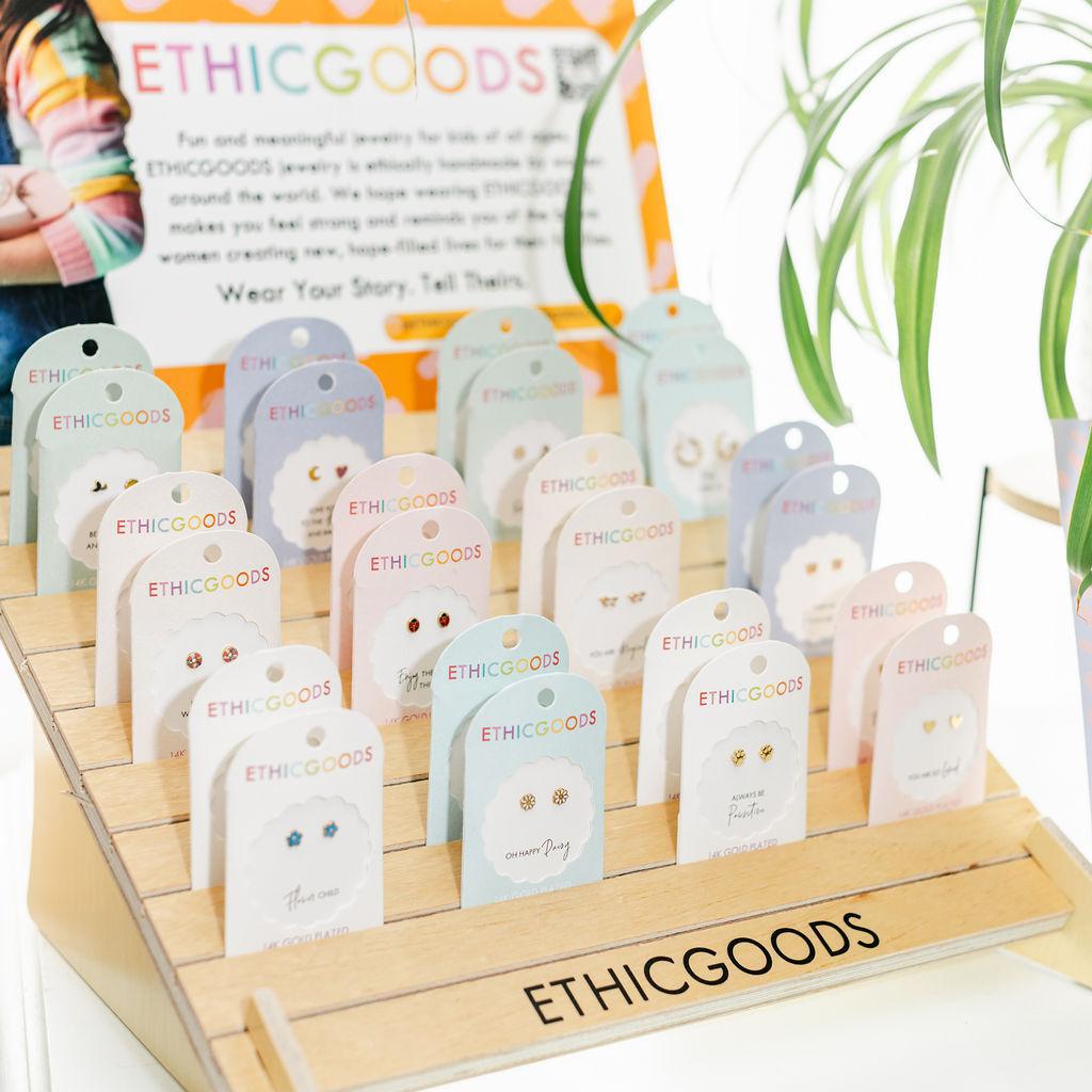 Display of ETHICGOODS jewelry with branded tags on a wooden stand.
