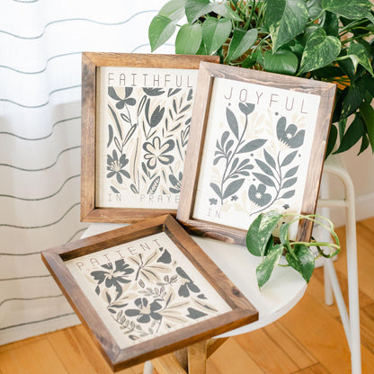 Three framed prints with motivational phrases on a table with plants in the background