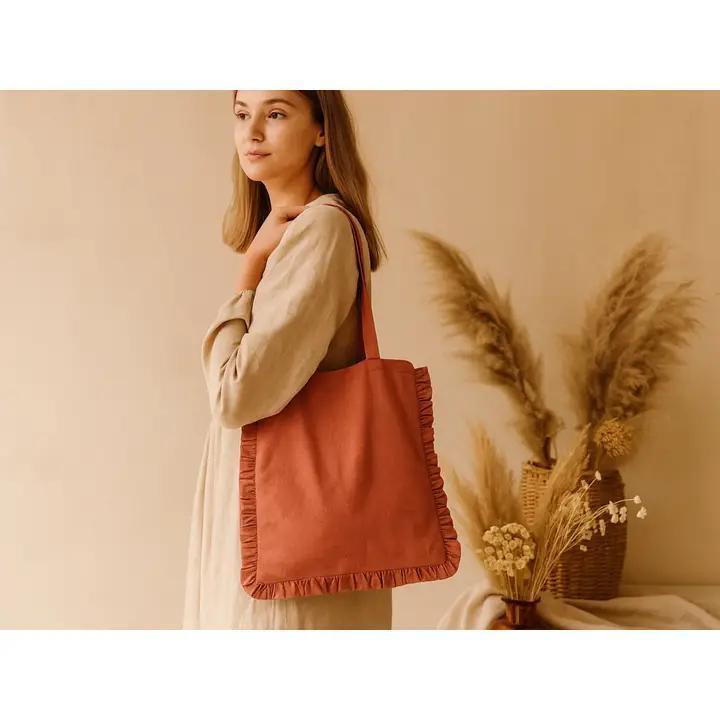Woman holding a terracotta-colored tote bag with decorative elements against a beige background.