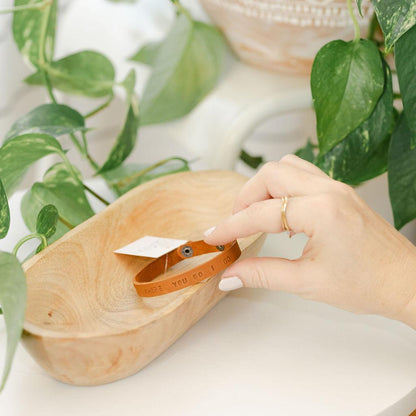 Hand holding a light brown leather bracelet with &