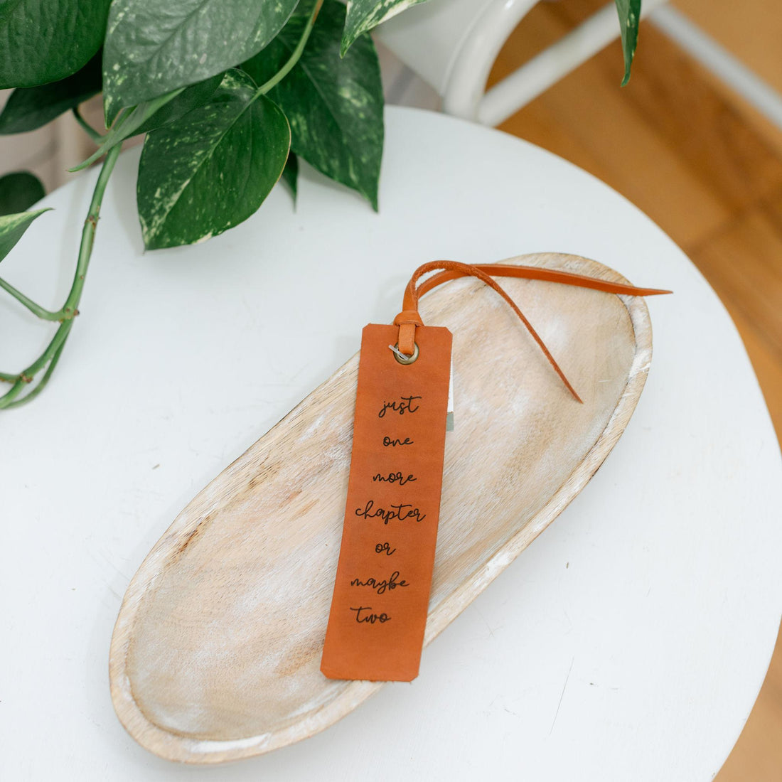 Leather bookmark with text on a wooden surface with a plant in the background