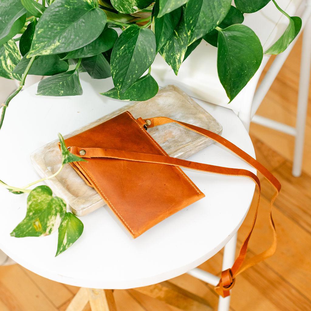 A small leather handbag on a wooden surface with a plant in the background