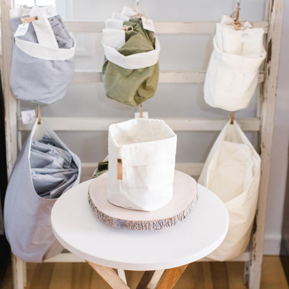 Storage solution with hanging fabric bins filled with a stack of folded bins. One cream bin in the front on a table